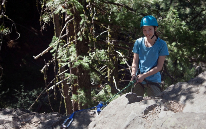 an outward bound student wearing rock climbing gear smiles at the camera 